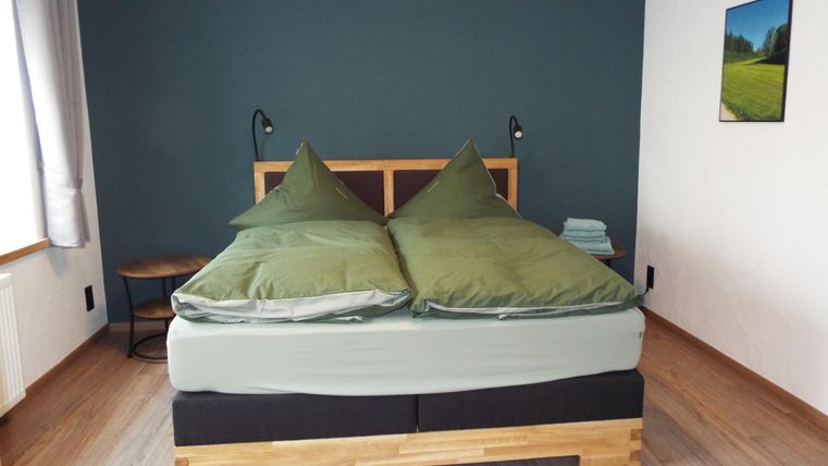 Ein gemütliches Schlafzimmer mit einem großen Bett und zwei grünen Kissen. Die Wände sind in einem dunklen Farbton gestrichen, und ein Bild hängt an der Wand.
