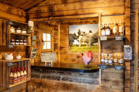 Ein gemütlicher Verkaufsraum aus Holz mit Regalen voller Lebensmittel und Getränken. An der Wand hängt ein Bild von Kühen auf einer Wiese.