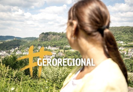 Een vrouw op de voorgrond kijkt naar de stad Gerolstein. Daarvoor staat het opschrift &ldquo;#GEROREGIONAL&rdquo;.