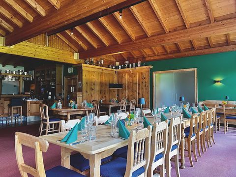 In einem Raum mit Holzdecke steht eine lange Holztafel, die in der Farbe grün eigededeckt ist, Im Hintergrund sind weitere gedeckte Tische