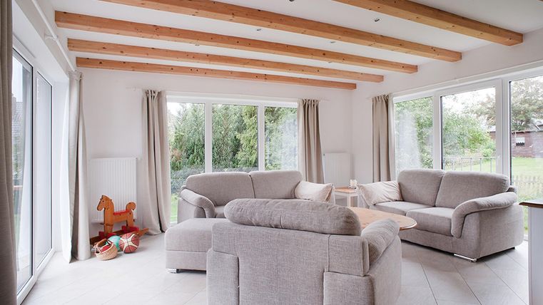 Ein helles Wohnzimmer mit großen Fenstern und einem Blick auf den Garten. Es gibt zwei gemütliche Sofas und einige Spielzeuge für Kinder.