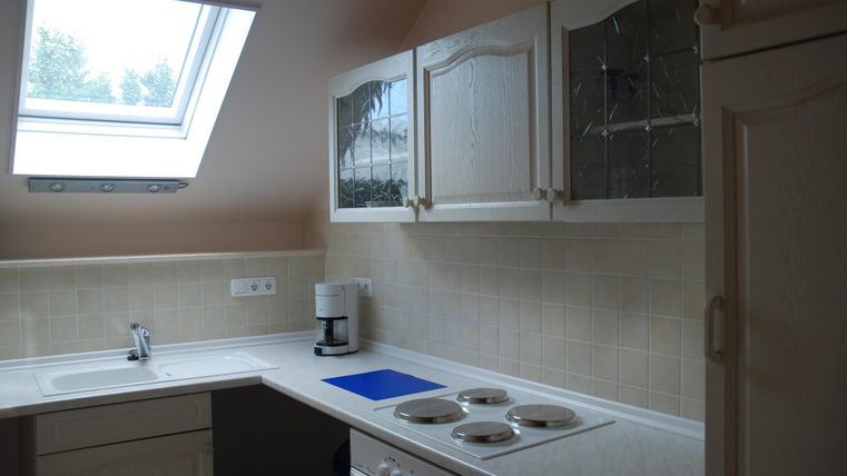 Eine moderne Küche mit weißen Schränken und einer großen Dachfenster. Die Arbeitsfläche ist hell und gut ausgestattet mit einem Herd und weiteren Geräten.