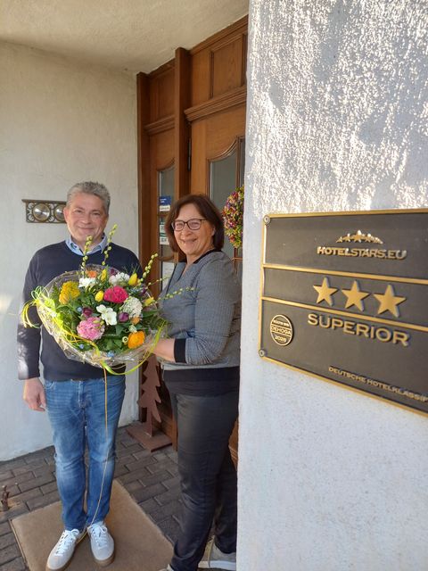 Zwei Personen halten einen Blumestrauß vor der Eingangstür des Landhauses.