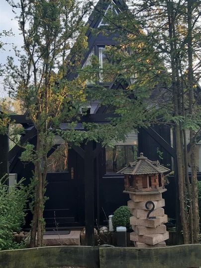 Ein großes, dunkles Holzhaus umgeben von hohen Bäumen. Im Vordergrund steht ein dekorativer Vogelhaus.