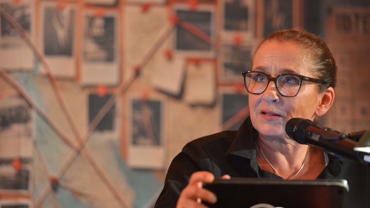 Eine Frau sitzt an einem Tisch und spricht in ein Mikrophon.