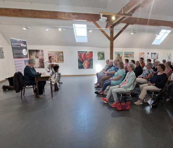 Zahlreiche Personen sitzen in Reihen hintereinander mit Blick zur krimi-Autorin Andrea Revers.