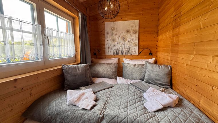 Ein gemütliches Schlafzimmer mit Holzverkleidung und einem großen Bett. Kissen und frische Handtücher sind ordentlich drapiert, während ein Kunstwerk an der Wand hängt.