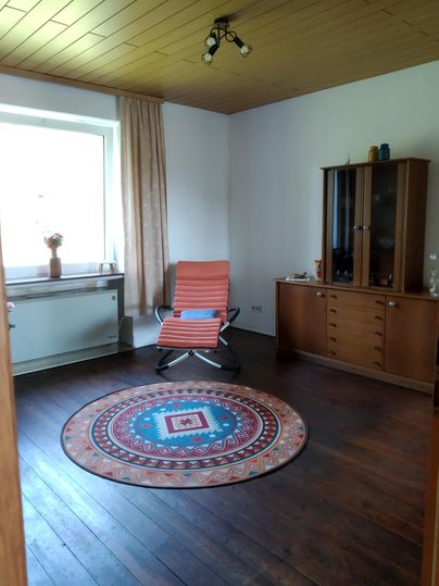 Une pièce confortable avec une chaise à rayures rouges et un tapis coloré. Il y a une fenêtre avec des rideaux et un buffet contre le mur.