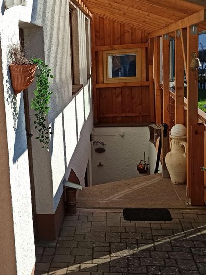 Une entrée accueillante avec des lambris en bois et un escalier confortable. Des plantes sont accrochées au mur, et au premier plan se trouve un récipient décoratif.