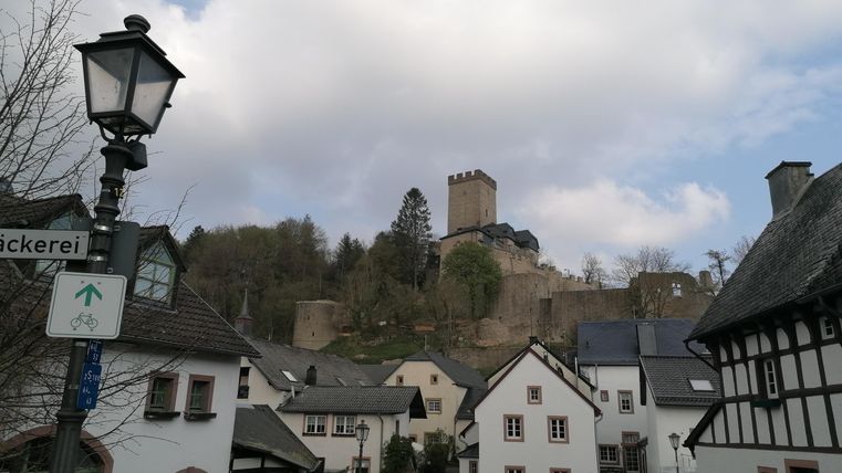 Eine malerische Stadtansicht mit traditionellen weißen Häusern und einer Burg im Hintergrund. Der Himmel ist bewölkt und es gibt eine Straßenlaterne im Vordergrund.
