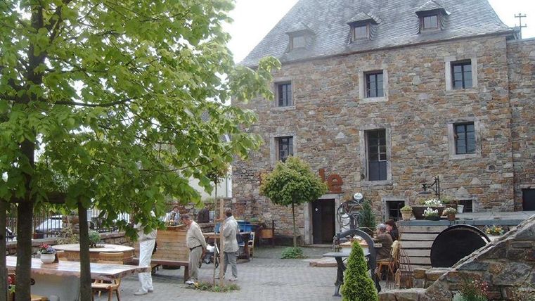 Ein großer Hof mit vielen Sitzbänken, Tischen und Bäumen. Dahinter ein großes Gebäude mit dem Schriftzug "Mühle" über der Eingangstür.