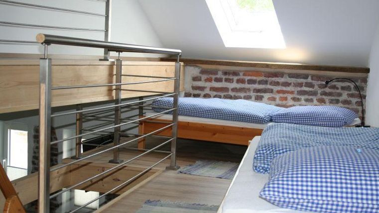 Een gezellige kamer met twee eenpersoonsbedden en een open balkon. De wanden zijn bekleed met bakstenen en het licht valt door een dakraam naar binnen.