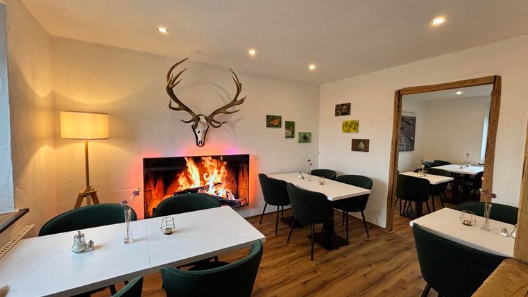 Ein gemütliches Restaurant mit einem offenen Kamin und stilvollen Tischen. Die Wände sind dekoriert mit Bildern und einem Geweih.