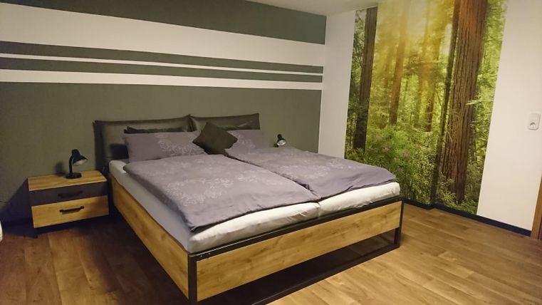 Une chambre moderne avec un grand lit et un cadre en bois. Les murs sont décorés de couleurs douces, et une fresque mural affiche une forêt.