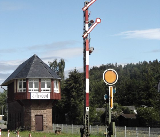 Old signal box building 'Lissendorf' and mechanical railroad signal in front of a blue sky, surrounded by green landscape., © Herr Schun