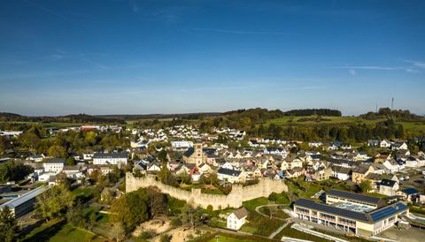 Luftaufnahme von Hillesheim mit historischer Stadtmauer und Kirche, umgeben von grüner Landschaft.