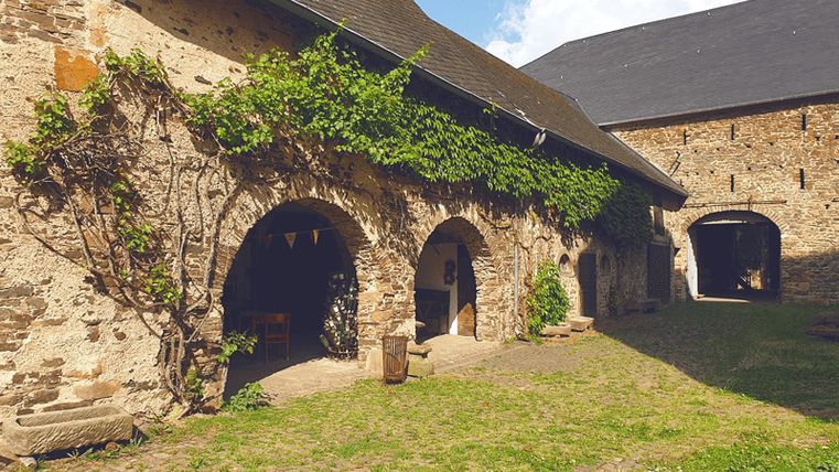 Innenhof der Unterburg Lissingen mit historischen Steinmauern, Bögen und Efeu bewachsen, bei sonnigem Wetter.