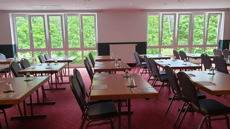 A bright conference room with tables and chairs. Large windows offer a view of the greenery.