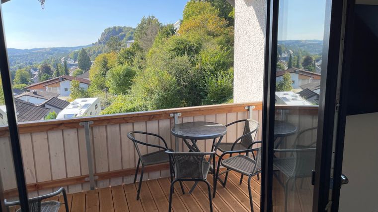 Un balcon confortable avec une table et des chaises. En arrière-plan, on aperçoit un paysage verdoyant et le ciel bleu.