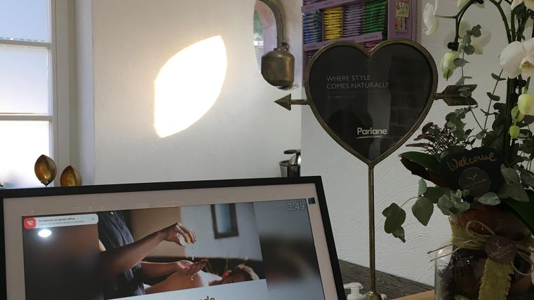 Un espace d'accueil moderne avec un écran affichant des informations sur les massages corporels Ayurvédiques. À côté, se trouve un présentoir en forme de cœur et des fleurs fraîches décorent le comptoir.