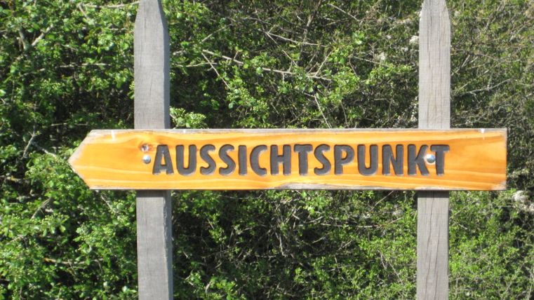 Holzschild mit der Aufschrift 'Aussichtspunkt' vor grünem Hintergrund.