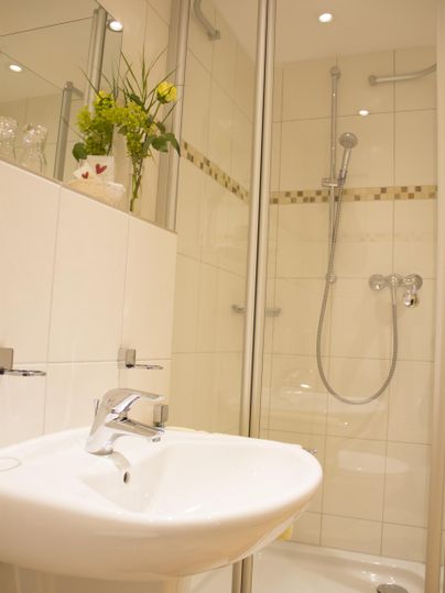 Ein modernes Badezimmer mit Dusche und Waschbecken. Weiße Fliesen und eine Pflanzen dekorieren den Raum.