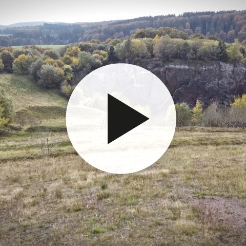 Landscape in the Steffeln Volcano Garden and the Steffelnberg volcano with video play button in the foreground.