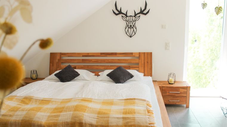 Ein helles Schlafzimmer mit einem großen Bett und einer gelben Decke. An der Wand hängt ein Hirschkopf als Dekoration.