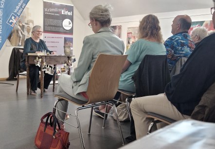 Zahlreiche Personen sitzen in Reihen hintereinander mit Blick zur Krimi-Autorin Andrea Revers.