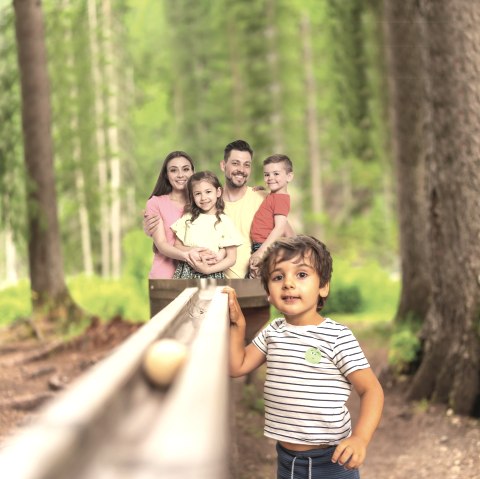 Eltern mit zwei Kindern auf dem Arm stehen hinter einer Hoz-Kugelbahn und ein Kind steht daneben im Wald.