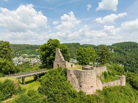 Luftaufnahme der Löwenburg mit der hinführenden Holzbrücke, umgeben von grüner Landschaft und Bäumen oberhalb von Gerolstein.