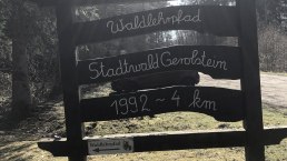 Holzschild mit der Aufschrift 'Waldlehrpfad Stadtwald Gerolstein 1992 ~ 4 km' im Wald bei Sonnenschein., © Touristik GmbH Gerolsteiner Land,Leonie Post