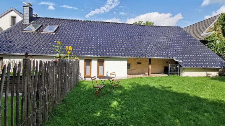 Een modern huis met een blauw dak en een groen onderhouden tuin. In de tuin staan twee stoelen op het gras.