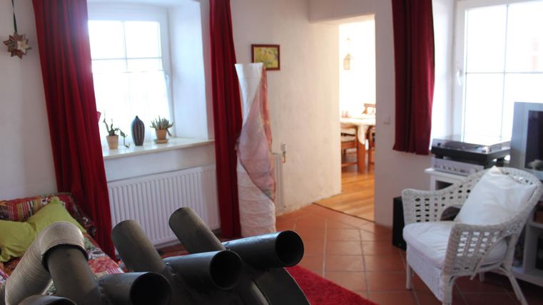 Een uitnodigende woonkamer met rode gordijnen, een comfortabele bank en een televisie. Op de achtergrond is een eethoek zichtbaar.