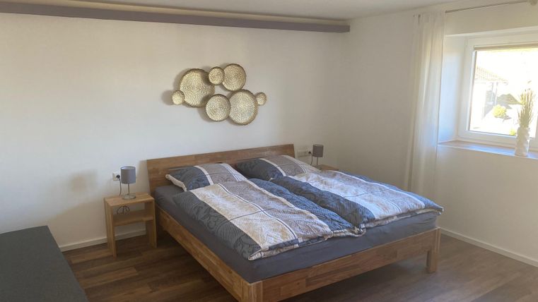 Ein gemütliches Schlafzimmer mit einem großen Holzbett und einer schönen Bettdecke. Ein Fenster lässt viel Licht herein und sorgt für eine helle Atmosphäre.