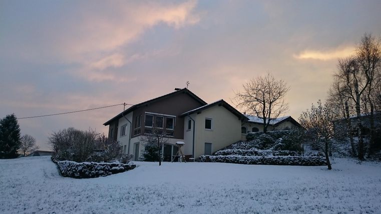 Ein schönes Haus umgeben von Schnee. Der Himmel ist pastellfarben und wolkig.