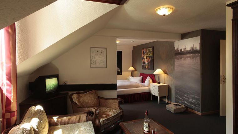 Une chambre d'hôtel confortable avec un coin salon et un coin nuit. Elle dispose de meubles en bois, d'une télévision et d'éléments décoratifs aux murs.