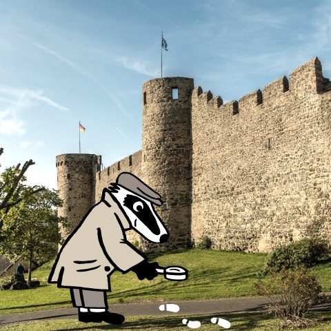 The high Hillesheim town wall stands in front of a green area under a blue sky. On a narrow path in front of the wall, Detective Badger examines white footprints with a magnifying glass.