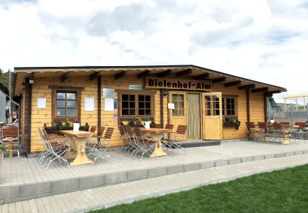 Wooden building with a terrace and several tables and chairs in front of it. 