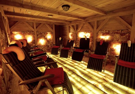 Ein dunkler Raum mit einer Holzdecke und W&auml;nden aus Salzsteinen. In dem Raum stehen mehrere Liegen.