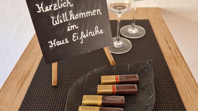A welcome sign stands on a table, surrounded by champagne glasses. On a sheet, chocolate bars are laid out in various colors.