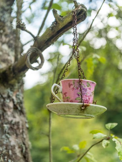 Eine rosa Tasse mit Blumenmuster hängt an einer Kette an einem Ast.
