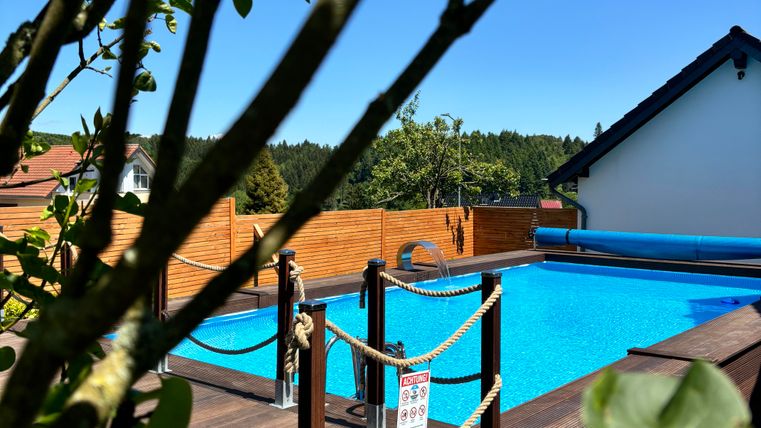 Ein schöner Pool umgeben von Holzterrasse und Bäumen. Der klare blaue Himmel sorgt für eine einladende Atmosphäre.