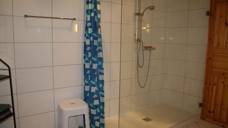 Een moderne badkamer met een inloopdouche en een douchegordijn. Een krukje staat naast de douche en er is een houten kast op de achtergrond.