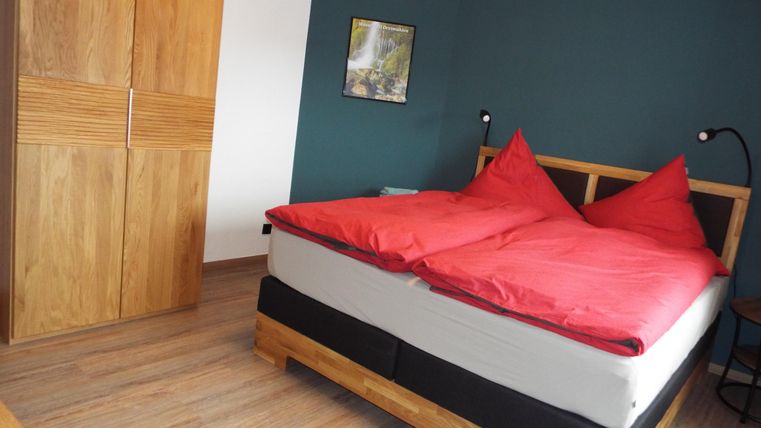Ein gemütliches Schlafzimmer mit einem großen Bett und roten Kissen. Der Raum hat einen Holzschrank und eine grüne Wand.