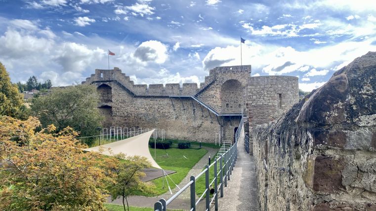 Begehbare hohe Stadtmauer aus Stein in Hillesheim mit angrenzender Parkfläche.