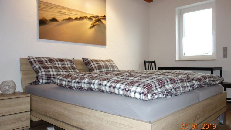 Ein gemütliches Schlafzimmer mit einem großen Bett und karierten Bettwäsche. An der Wand hängt ein Bild von einer Küstenlandschaft.