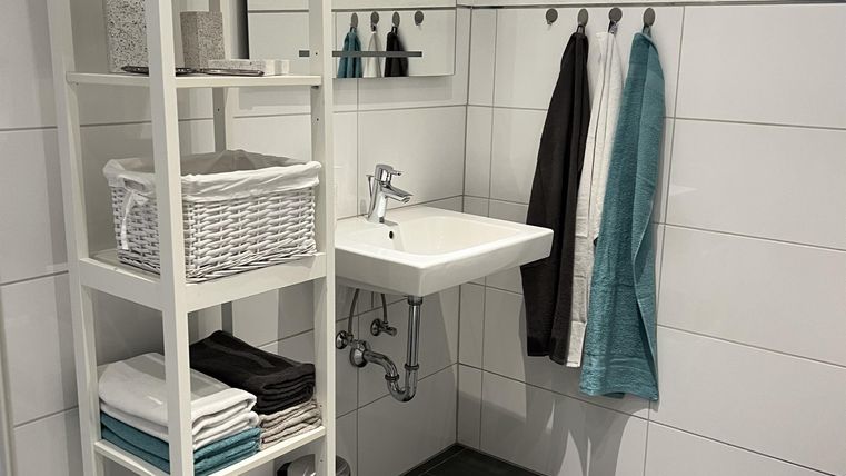 Een moderne badkamer met een witte plank en een wastafel. Handdoeken en verzorgingsproducten zijn netjes gerangschikt.