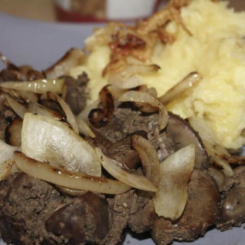 Meat and onion preparation with a pile of mashed potatoes on the side.