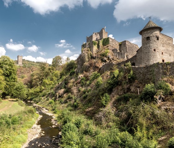 De kastelen van Manderscheid troon op een heuvel in het midden van een groen landschap, omringd door bomen en een kleine rivier onder een blauwe hemel., © Dominik Ketz